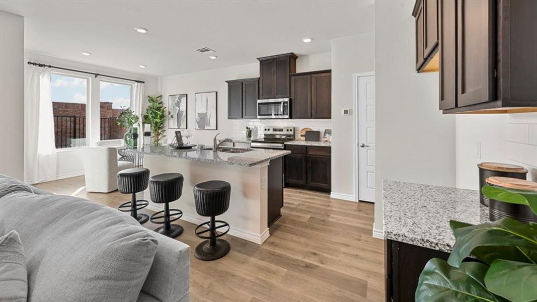Kitchen featuring light stone counters, a breakfast bar area, a center island with sink, appliances with stainless steel finishes, and dark brown cabinetry Kitchen featuring light stone counters, a breakfast bar area, a center island with sink, appliances with stainless steel finishes, and dark brown cabinetry