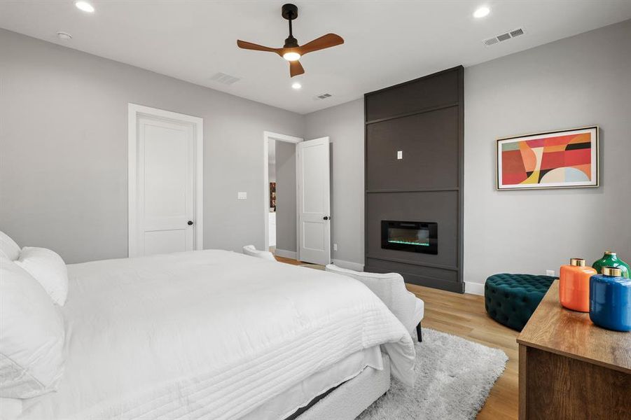 Bedroom with ceiling fan, a fireplace, and light hardwood / wood-style floors