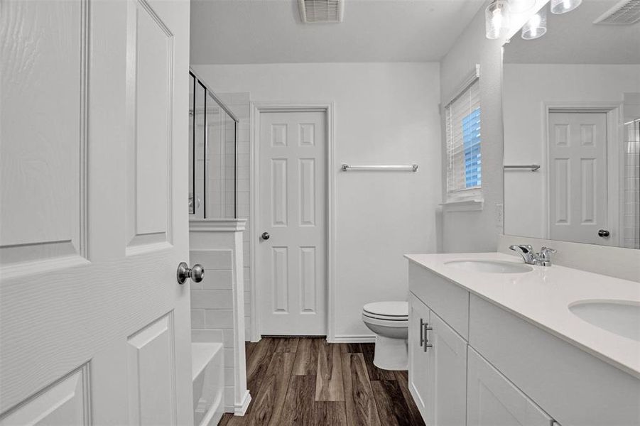 Bathroom featuring a double vanity with white countertops and integrated sinks, wood-finish flooring, a white paneled door, and a shower enclosure with glass panels and subway tile