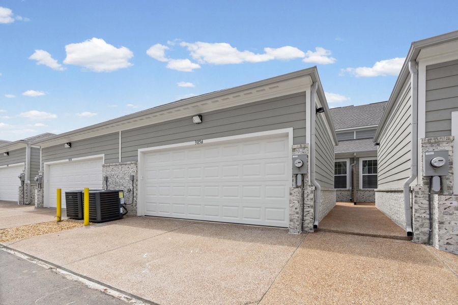 Individual garage parking with panel doors, gray siding, stone accent facade, and concrete driveways