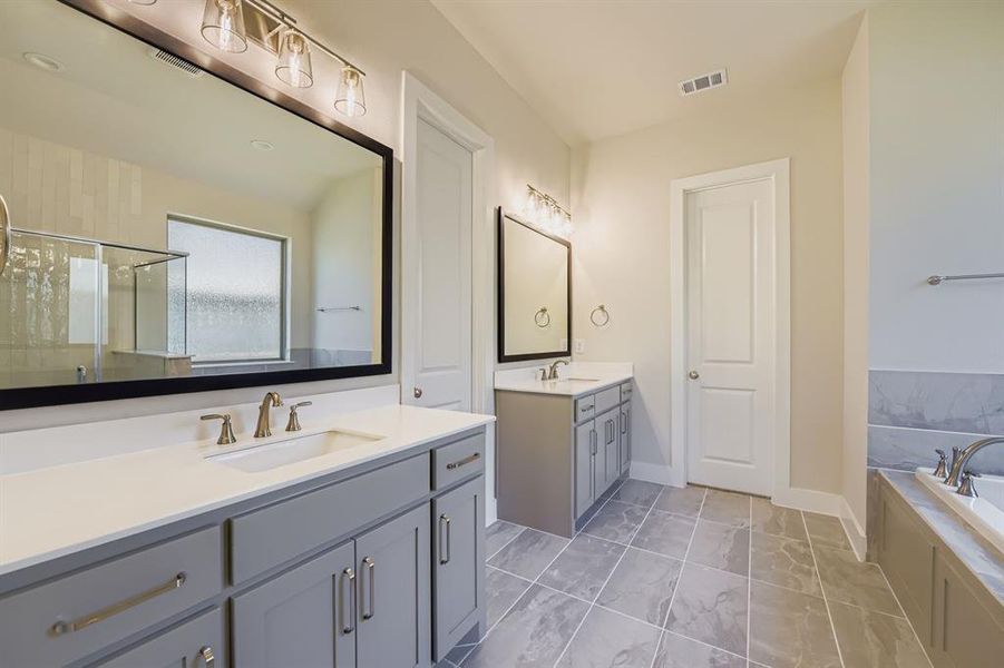 Bathroom featuring a stall shower, two vanities, a garden tub, and light marble finish floors
