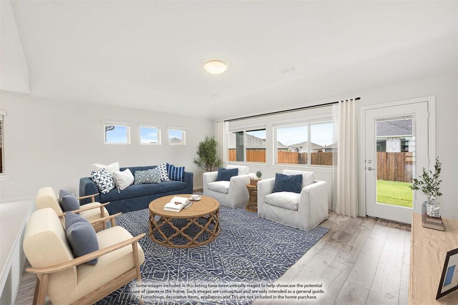 Living room with light wood floors, blue sofa, white chairs, and large windows with backyard view
