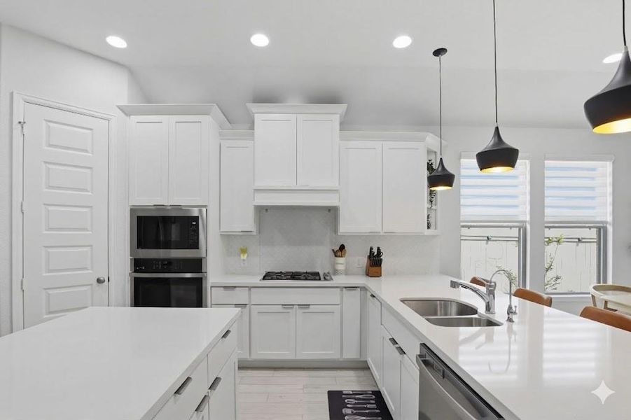A detailed view of the kitchen workspaces highlighting the quartz countertops, stainless under-mount sink, and modern black pendant lights.