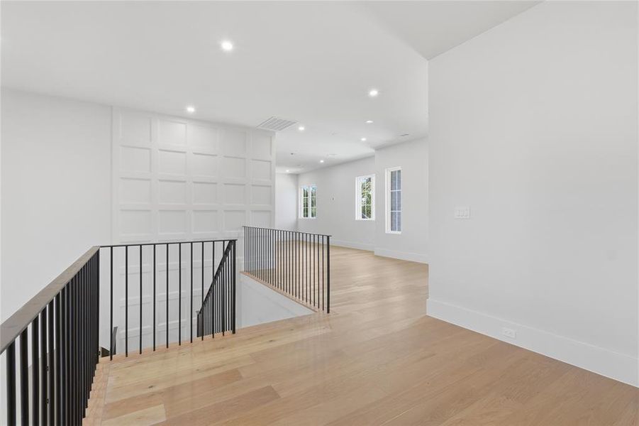 Open second-floor landing with board-and-batten accent wall, black iron railing, and hardwood floors Open second-floor landing with board-and-batten accent wall, black iron railing, and hardwood floors