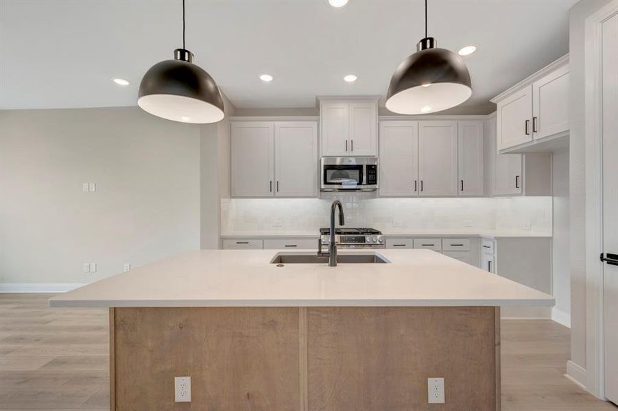 Kitchen with an island with sink, decorative backsplash, stainless steel appliances, light wood-style floors, and two tone cabinets