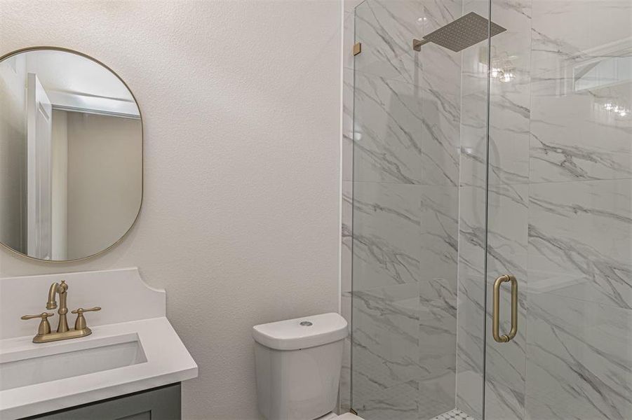 Bathroom featuring a walk-in shower with clear glass enclosure and marble-look tile walls, a rain showerhead, a vanity with a white countertop and undermount sink, a bronze-finish faucet, and an oval mirror