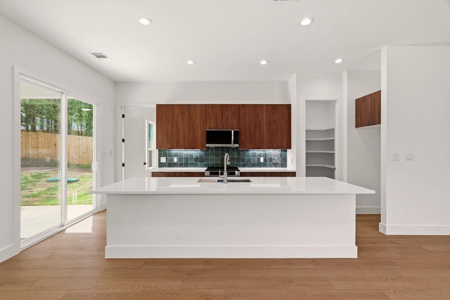Kitchen with modern cabinets, light wood finished floors, a kitchen island with sink, light stone countertops, and recessed lighting