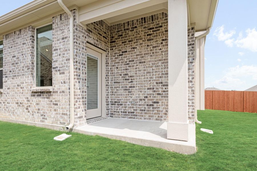 Brick home exterior with covered back patio, concrete slab, green lawn, and wood privacy fence.