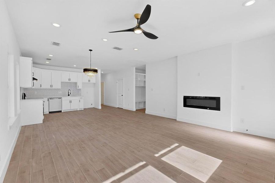 Unfurnished living room featuring recessed lighting, a chandelier, light wood-style floors, a glass covered fireplace, and ceiling fan