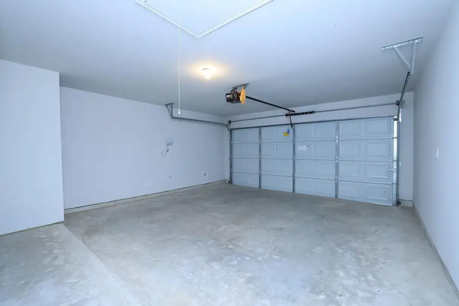 The two-car garage features a concrete floor, white walls, and a large automatic door. It's well-lit and offers ample storage or parking space.