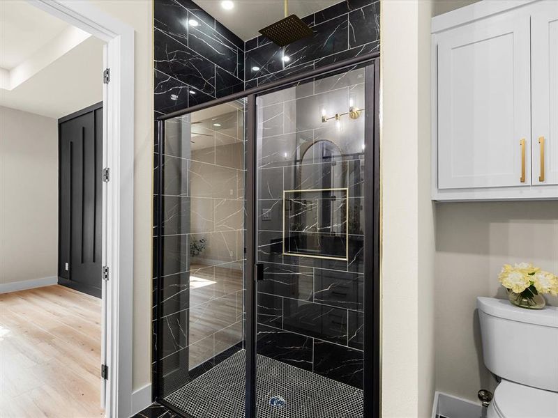 Modern shower enclosure featuring black marble-style tile, a black penny tile floor, and a black framed glass door