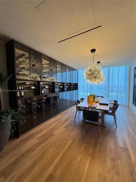 Floor-to-ceiling custom wine storage with glass-panel cabinetry, wood-finish flooring, statement globe chandelier, and expansive windows
