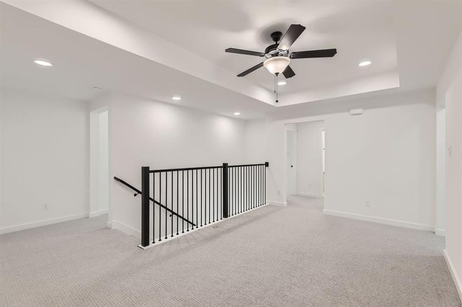 Carpeted empty room with ceiling fan and a tray ceiling