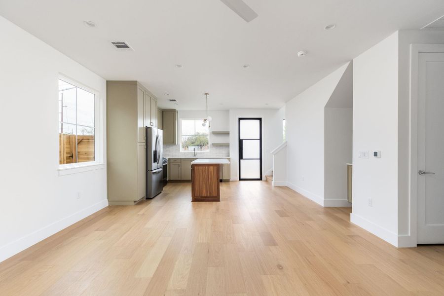Kitchen featuring open floor plan, a center island, light countertops, light wood finished floors, and stainless steel refrigerator with ice dispenser