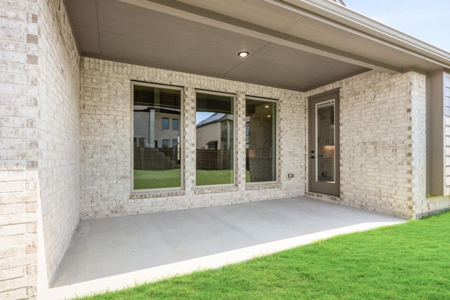 Covered back patio with concrete floor, light brick walls, large windows, and a back door leading inside