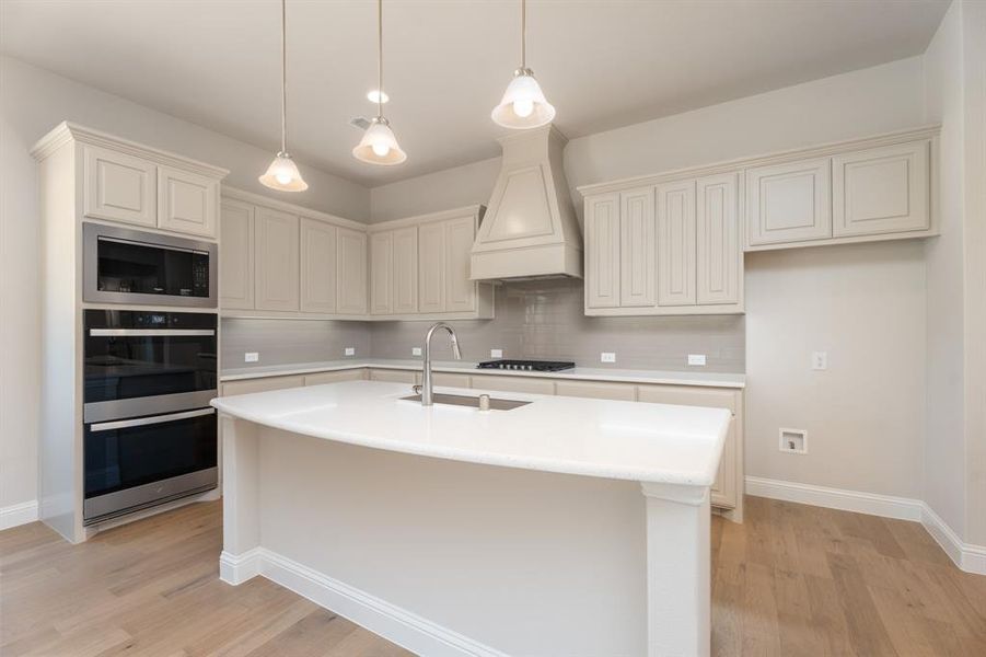 Kitchen with light wood-style flooring, pendant lighting, stainless steel appliances, decorative backsplash, and custom exhaust hood