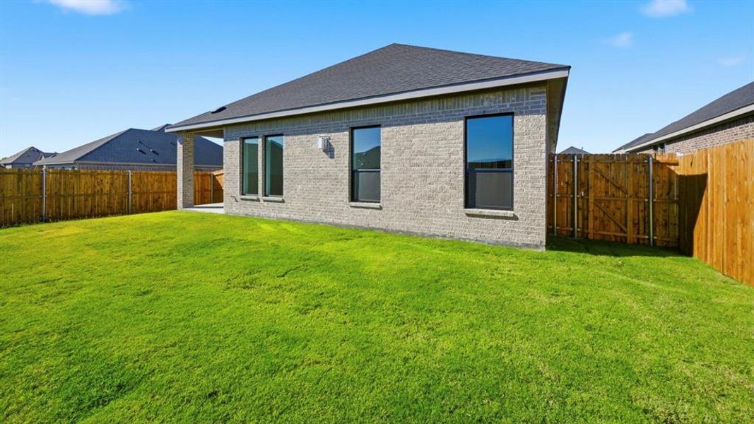 Back of house featuring brick siding, a fenced backyard, roof with shingles, and a gate