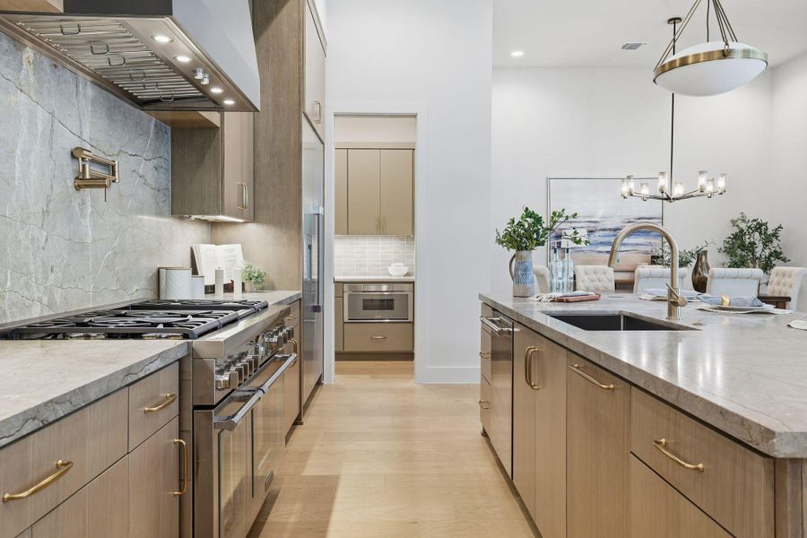 Kitchen with high end appliances, wall chimney range hood, decorative backsplash, hanging light fixtures, and recessed lighting