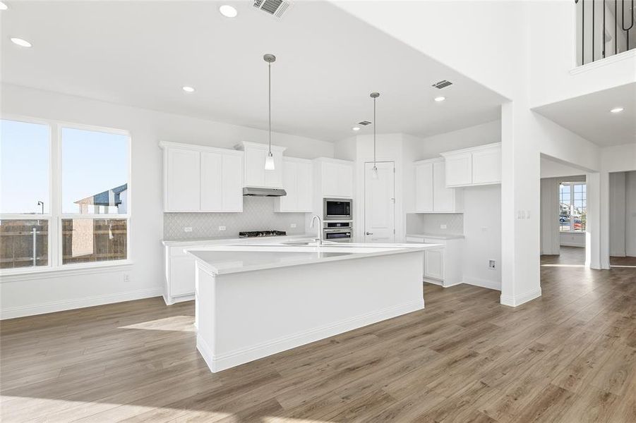Kitchen featuring white cabinets, a center island with sink, light wood-type flooring, decorative light fixtures, and light stone countertops Kitchen featuring white cabinets, a center island with sink, light wood-type flooring, decorative light fixtures, and light stone countertops