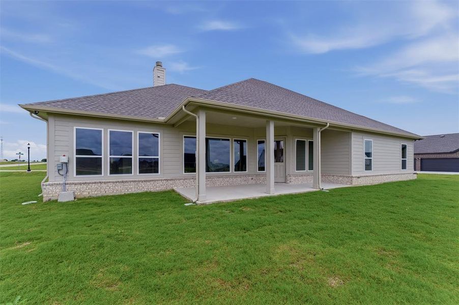 Rear elevation featuring a covered patio with columns, multiple large windows, and a chimney