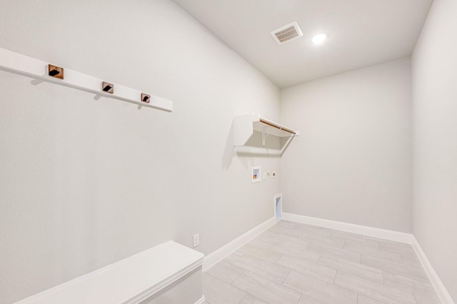 Laundry room with wall-mounted shelf, hanging rod, washer hookups, and light tile flooring Laundry room with wall-mounted shelf, hanging rod, washer hookups, and light tile flooring