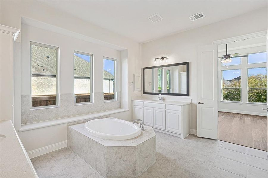 Bathroom with tiled bath, ceiling fan, tile patterned flooring, and vanity