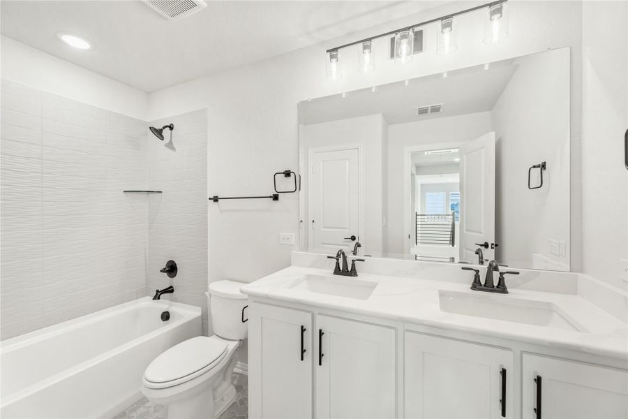 Bathroom with double sink vanity, white cabinets, tub-shower combo, and black hardware accents