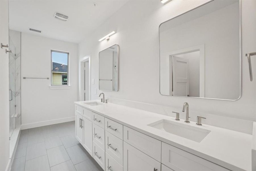 Full bath with a marble finish shower, double vanity, and light tile patterned floors