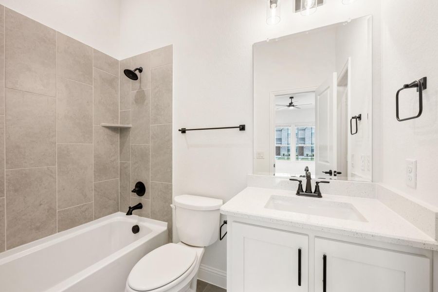 Bathroom with tiled tub and shower, white vanity with quartz countertop, and black hardware fixtures