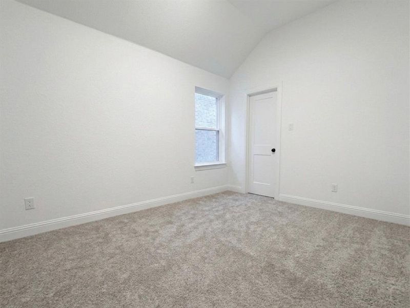 Spacious room featuring vaulted ceilings, light gray carpet, white baseboards, and a white interior door with a black knob