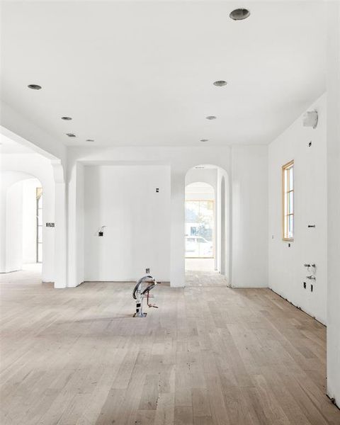 Unfurnished living room with arched walkways, light wood-style floors, plenty of natural light, and recessed lighting