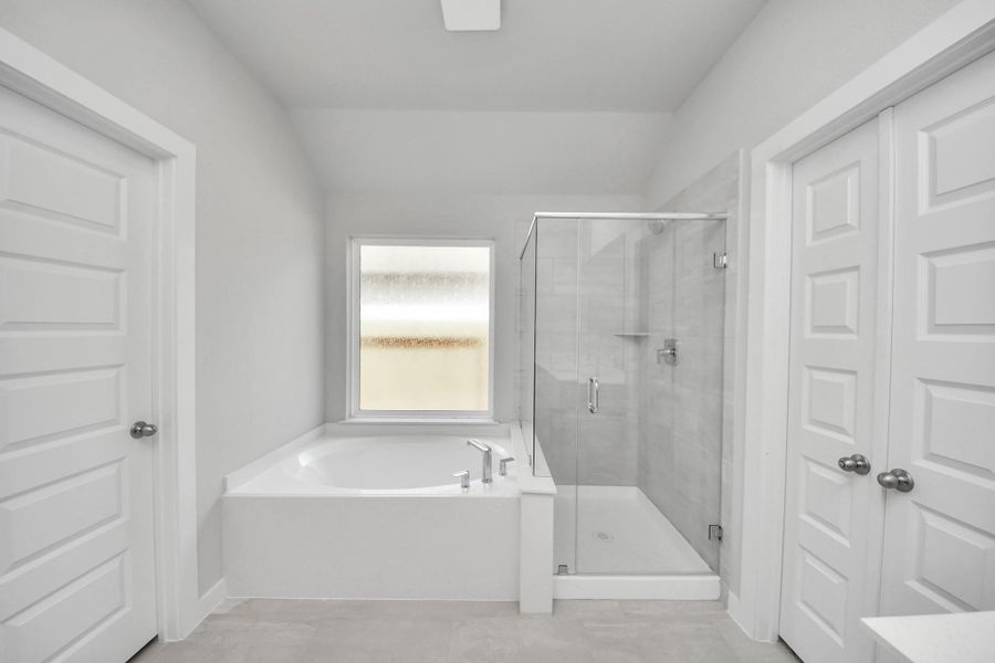 Indulge in a spa-like retreat within the confines of this primary bathroom. Delight in a spacious walk-in shower enveloped in stylish tile surround and unwind in a separate garden tub adorned with custom detailing. Sample photo of completed home with similar floor plan. Actual colors and selections may vary.