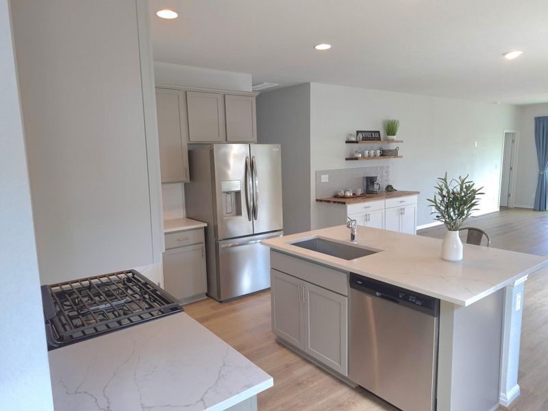 Kitchen featuring gray cabinetry, light wood-type flooring, stainless steel appliances, light stone countertops, and a kitchen island with sink