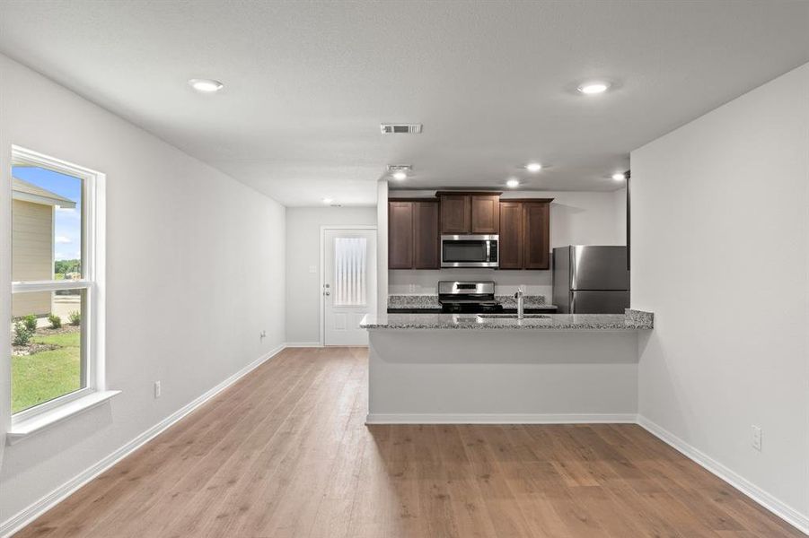 Kitchen featuring dark brown cabinets, a peninsula, stainless steel appliances, light stone countertops, and light wood-type flooring Kitchen featuring dark brown cabinets, a peninsula, stainless steel appliances, light stone countertops, and light wood-type flooring
