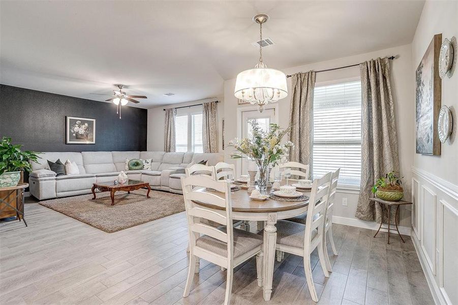 Dining space with light wood finished floors, visible vents, and ceiling fan with notable chandelier