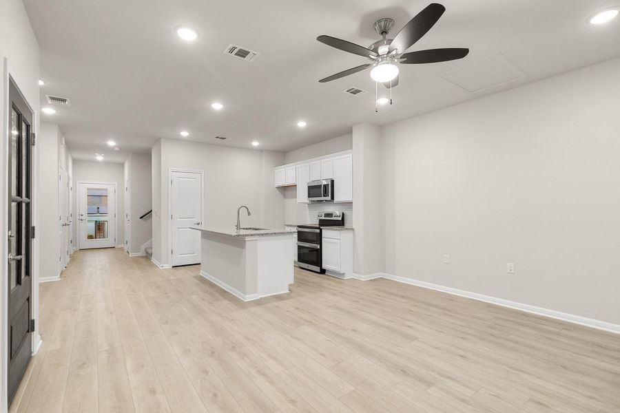 The open-plan living space features light-colored flooring, recessed lighting, and a modern ceiling fan