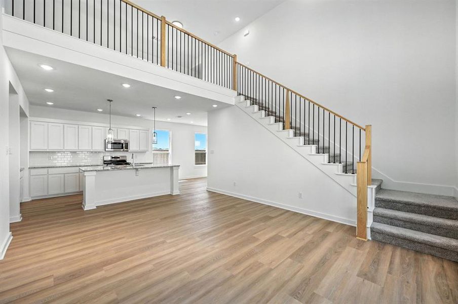 Unfurnished living room featuring a high ceiling, stairway, light wood-style floors, and recessed lighting