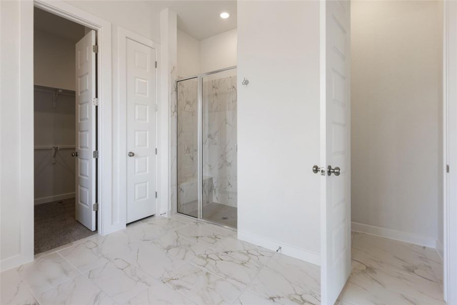 Bathroom featuring a marble finish shower, light marble finish floors, a spacious closet, and recessed lighting