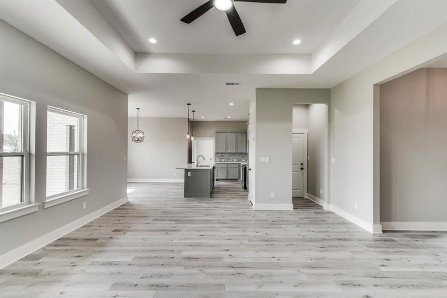 Unfurnished living room featuring ceiling fan, light hardwood / wood-style flooring, a raised ceiling, and sink