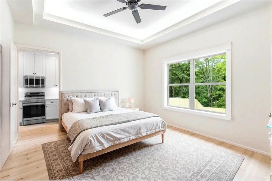 Bedroom featuring a raised ceiling, light wood-style flooring, and ceiling fan
