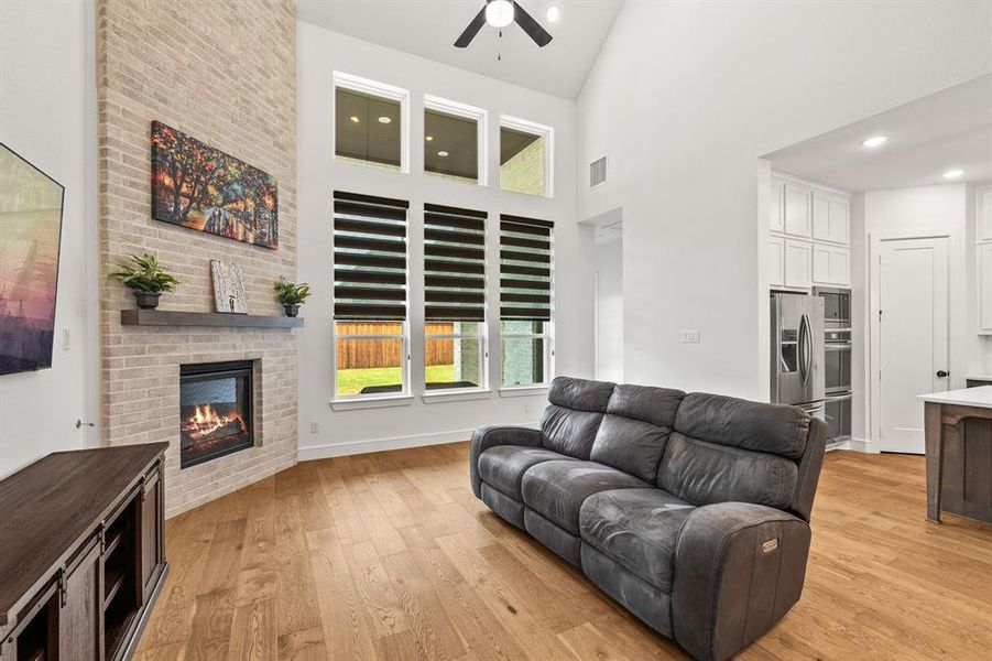 Living area featuring a towering ceiling, light wood-style floors, a brick fireplace, a ceiling fan, and recessed lighting Living area featuring a towering ceiling, light wood-style floors, a brick fireplace, a ceiling fan, and recessed lighting