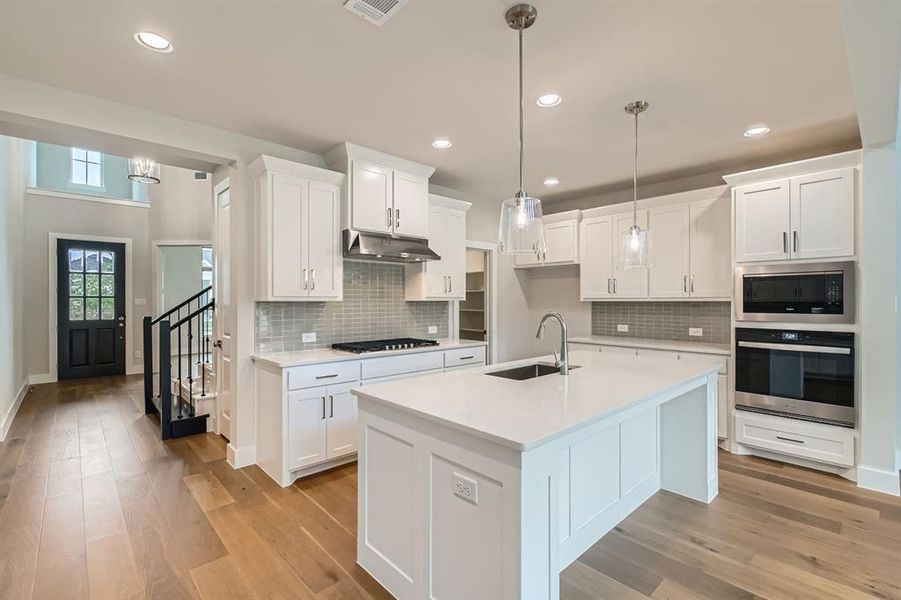 Kitchen featuring stainless steel appliances, under cabinet range hood, light countertops, light wood-style floors, and backsplash Kitchen featuring stainless steel appliances, under cabinet range hood, light countertops, light wood-style floors, and backsplash