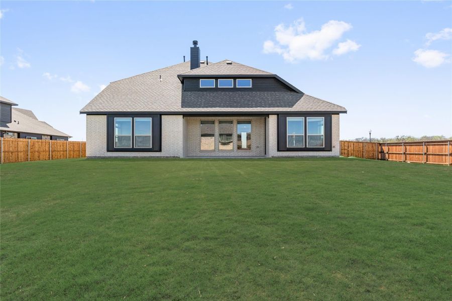 Rear view of brick home with large windows, covered patio, and fenced backyard with green lawn Rear view of brick home with large windows, covered patio, and fenced backyard with green lawn