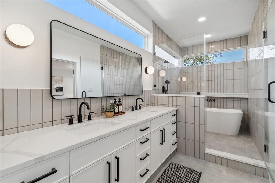 Stunning spa-like primary bathroom featuring a dual vanity with sleek black hardware, a frameless glass shower, and a luxurious soaking tub, complemented by contemporary tile design and abundant natural light.