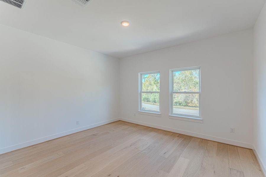 This bright, spacious room features light hardwood floors, two large windows providing natural light, and a neutral color palette, perfect for customization.