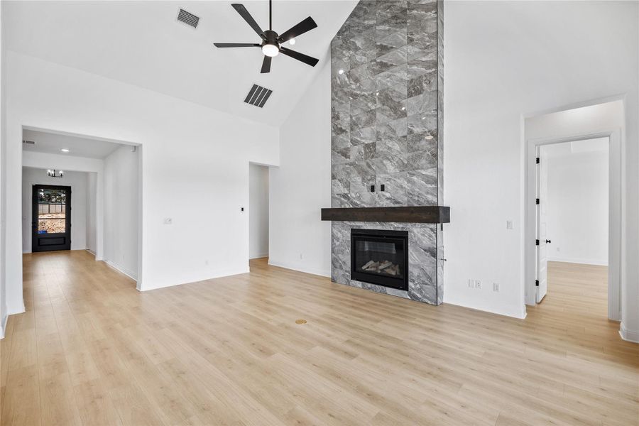 Unfurnished living room with a premium fireplace, a ceiling fan, light wood-style floors, and lofted ceiling