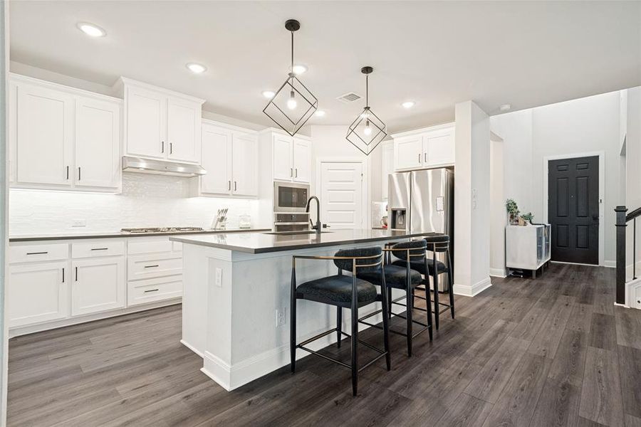 Modern kitchen featuring an island with seating, white cabinetry, dark countertops, and stainless steel appliances