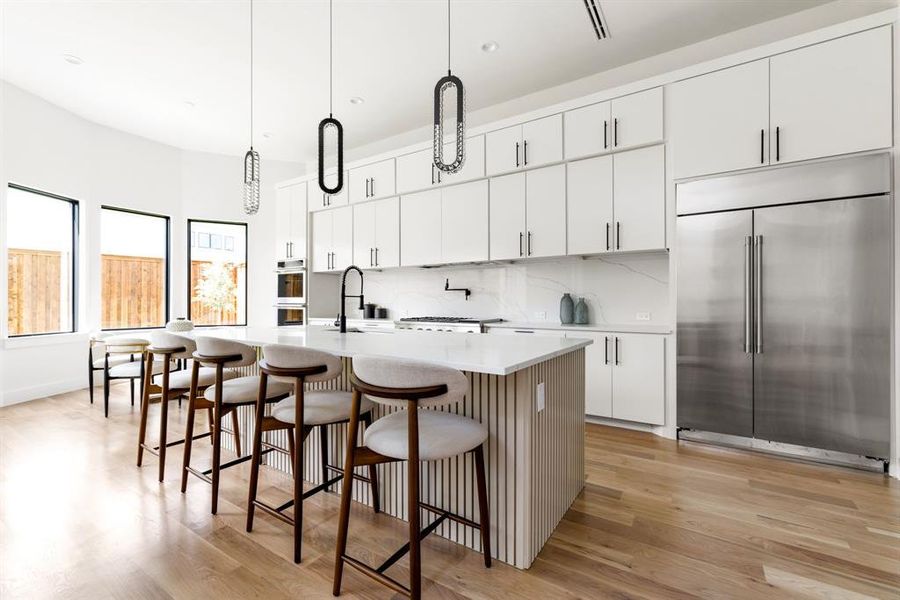 Kitchen featuring appliances with stainless steel finishes, light wood finished floors, an island with sink, light countertops, and tasteful backsplash Kitchen featuring appliances with stainless steel finishes, light wood finished floors, an island with sink, light countertops, and tasteful backsplash