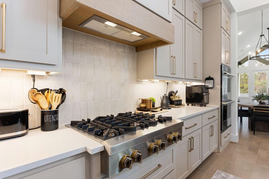 This modern kitchen with sleek white cabinetry, a spacious countertop, and a high-end gas stove. The room is well-lit with under-cabinet lighting and features stylish gold hardware.