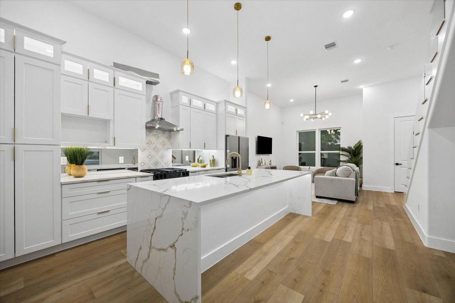 This modern kitchen and living area features sleek white cabinetry, a large marble island, and wood flooring. Pendant lights add warmth, while open shelving and high ceilings create a spacious feel. The area seamlessly connects to a cozy living space with a large window. This modern kitchen and living area features sleek white cabinetry, a large marble island, and wood flooring. Pendant lights add warmth, while open shelving and high ceilings create a spacious feel. The area seamlessly connects to a cozy living space with a large window.